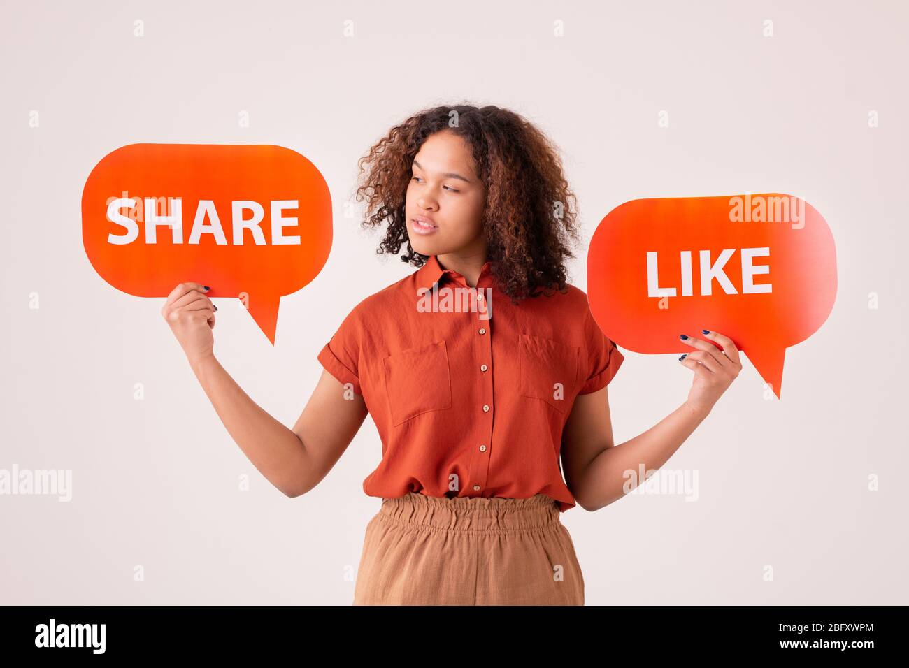 Nachdenkliche junge Afro-Amerikanerin, die Share and Like Tags hält und Social Media-Aktivitäten wählt Stockfoto