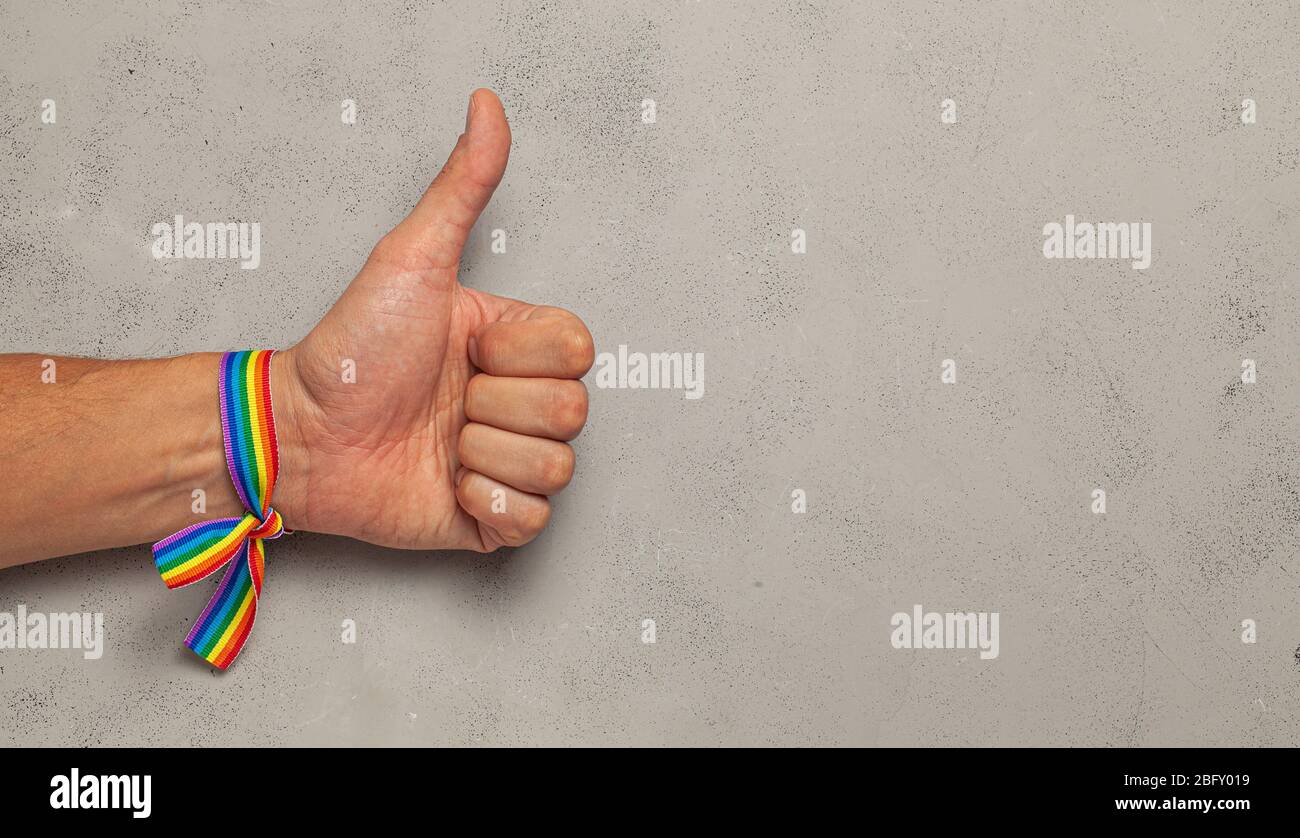 Daumen hoch. LGBT Regenbogen Band auf der männlichen Hand. Grauer Hintergrund Stockfoto