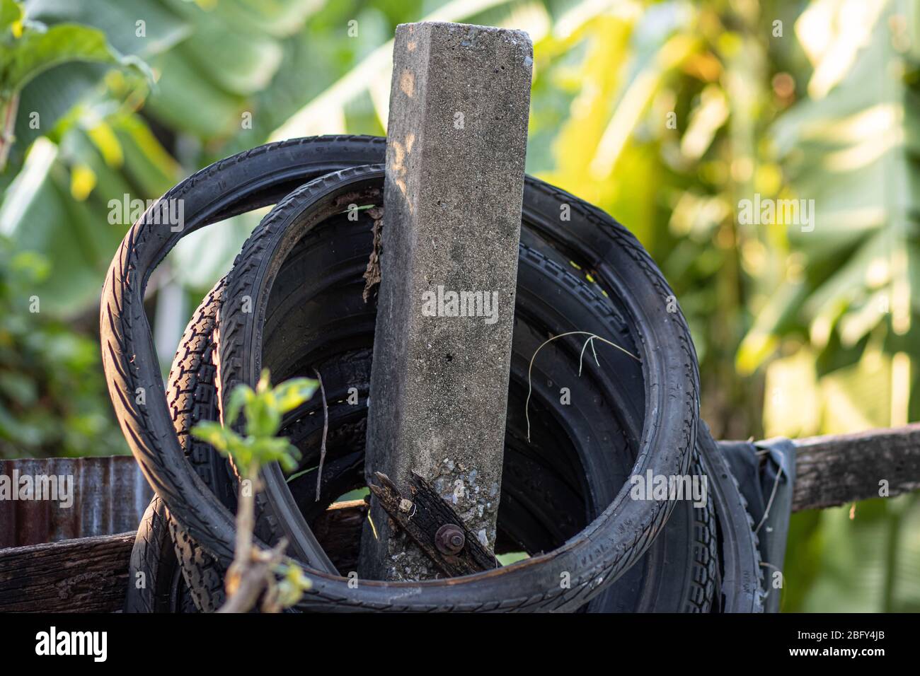 Ein alter gebrauchter Motorrad-Reifen hängt an der Säule vom Zaun im Hinterhof des thailändischen Haushalts. Stockfoto