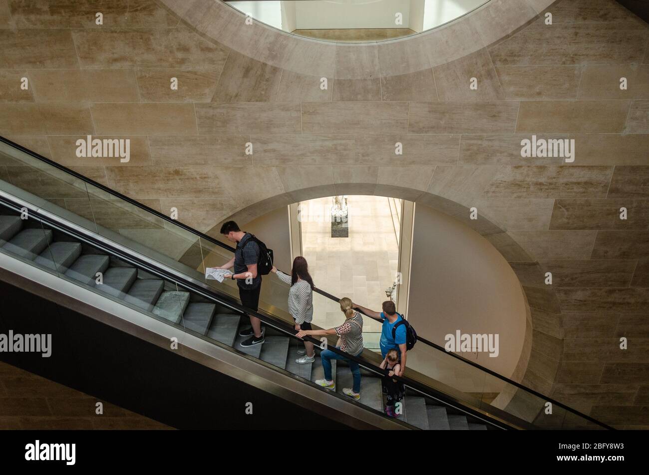 Konzept der Spiegelung (die unterbewusste Wiederholung der nonverbalen Signale einer anderen Person), die auf Touristen auf der Rolltreppe des Louvre, Paris, Frankreich, zu sehen ist Stockfoto