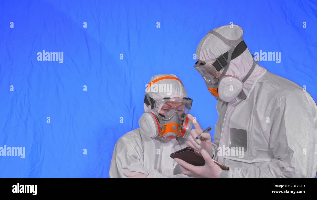 Wissenschaftler Virologe in Atemschutzgeräten schreibt in einem Tablet-Computer mit Eingabestift. Mann und Frau tragen eine medizinische Schutzmaske. Chroma Key blau. Stockfoto