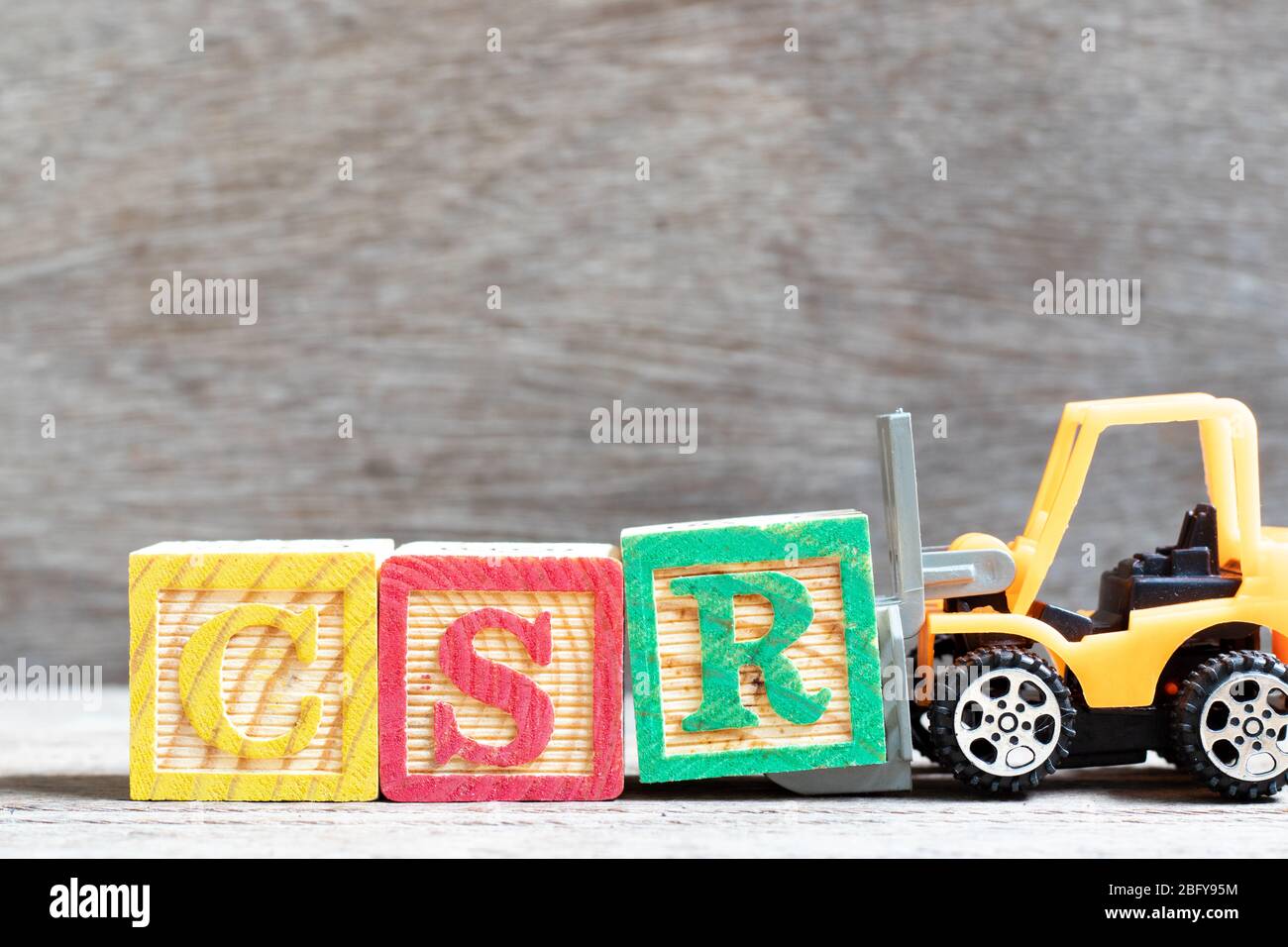 Spielzeug-Gabelstapler halten Buchstabenblock R in Wort CSR (Abkürzung von Corporate Social Responsibility) auf Holz Hintergrund Stockfoto