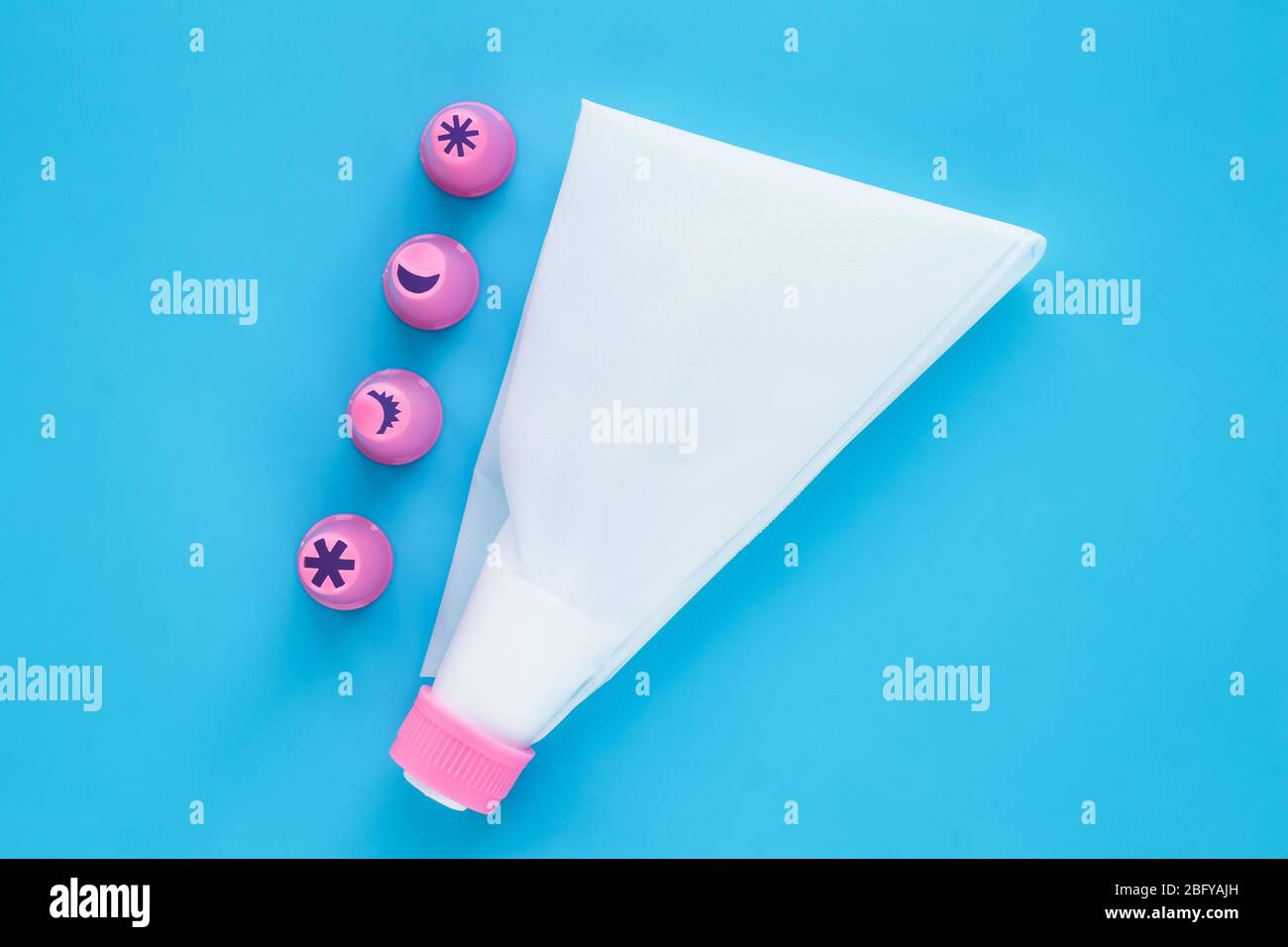 Kuchen dekorieren Werkzeuge auf blauem Hintergrund. Weißer Gebäckbeutel mit rosa Kunststoffdüsen zum Dekorationsbacken Stockfoto