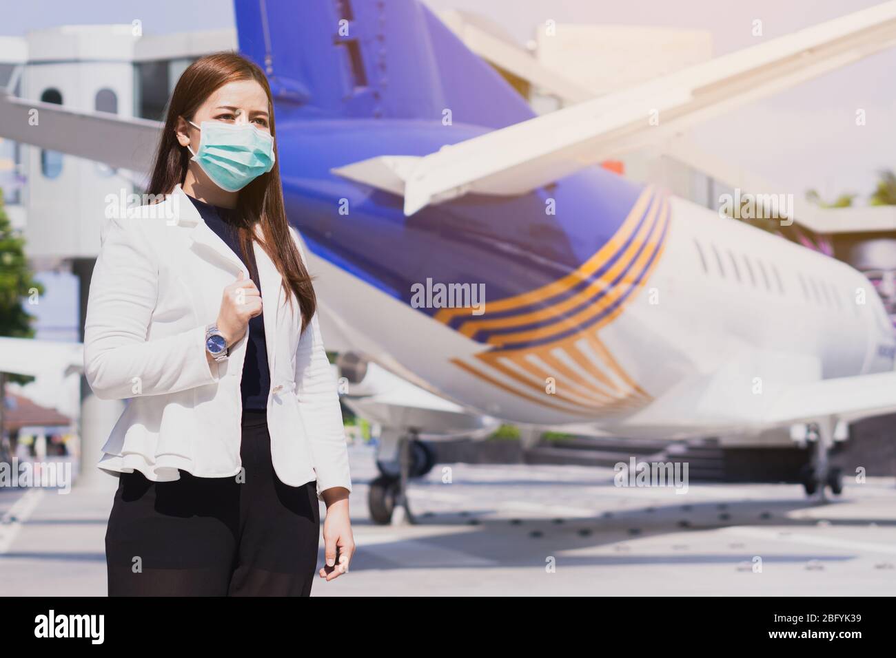 Die Geschäftsfrau lächelt und trägt eine Schutzmaske gegen Coronavirus, PM 2.5 und Kälte vor dem Flugzeug. Coronavirus und Air pol Stockfoto