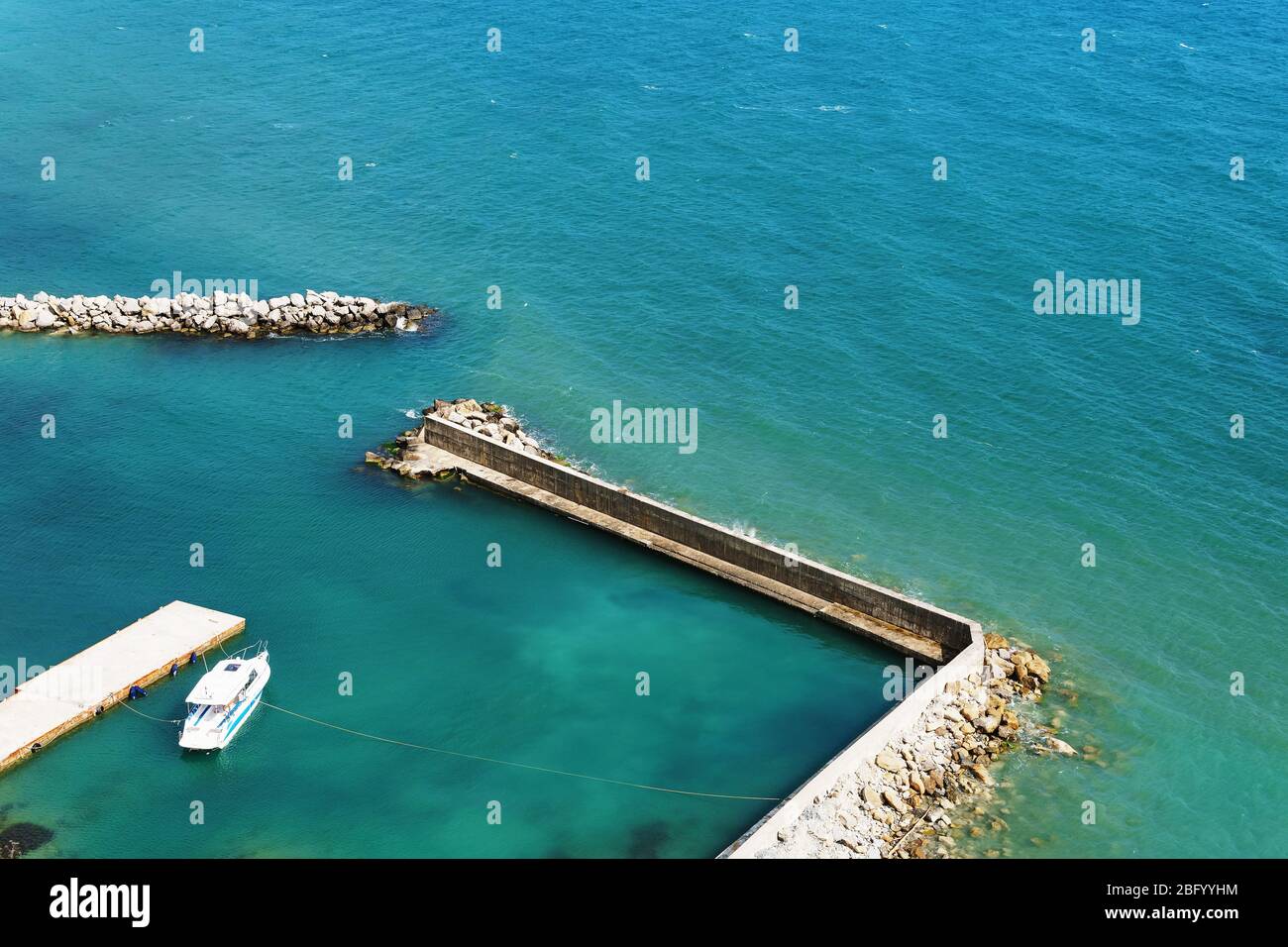 Ein einweisses Boot, das an einem sonnigen Tag am Meer festgemacht hat. Pier mit Zugang zum blauen Meer. Die Aussicht von oben Stockfoto