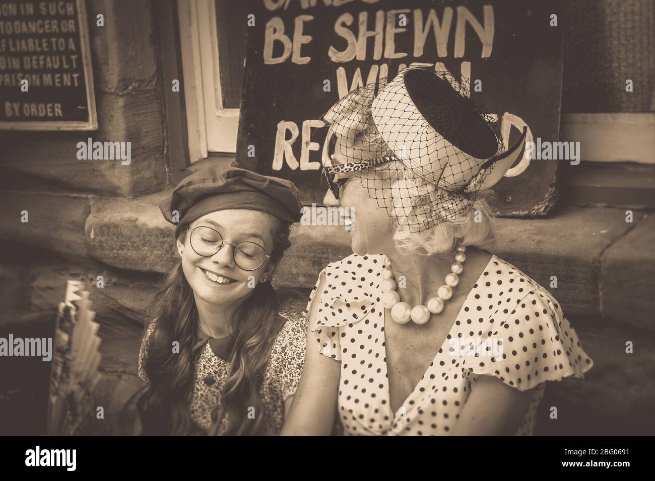 Vintage Sepia Nahaufnahme von 1940er Mädchen & 1940er Frau, Mutter & Tochter, am Vintage Bahnhof, Severn Valley Railway, WW2 war Zeit Sommer Event, Großbritannien. Stockfoto