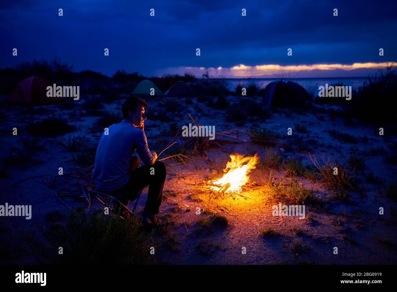 Mann, bei Lagerfeuer und Zelt in der Nacht am Strand des Sees Stockfoto