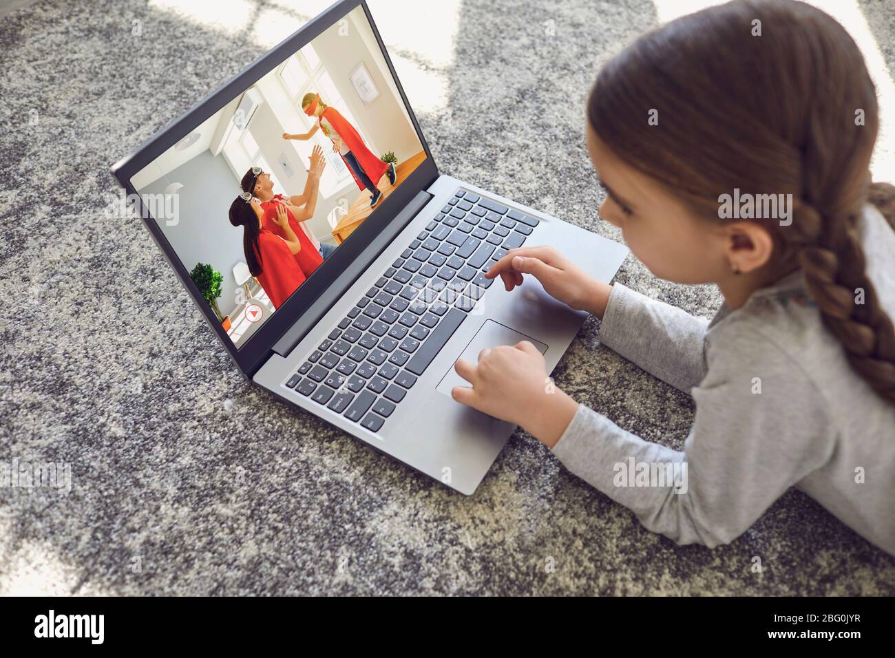 Ein Kind verwendet einen Laptop, um in einem Raum auf dem Boden Videos zu Hause anzusehen. Stockfoto