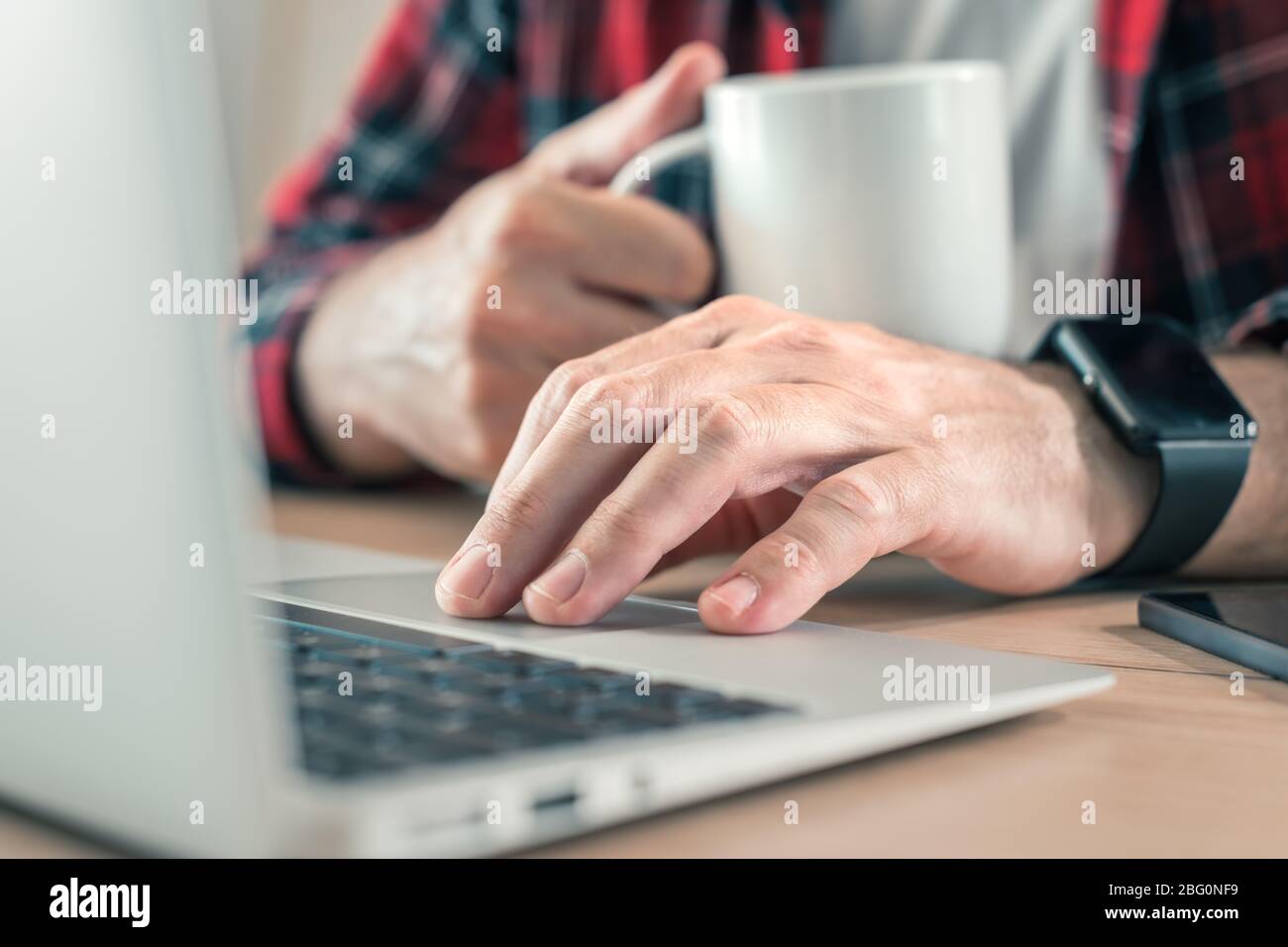 Freiberuflicher Mitarbeiter, der Laptop-Computer verwendet und Kaffee im Home Office trinkt, selektiver Fokus auf Hände Stockfoto