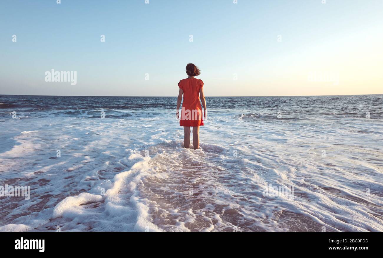 Frau im Meer bei Sonnenuntergang stehend, Farbtonierung angewendet. Stockfoto