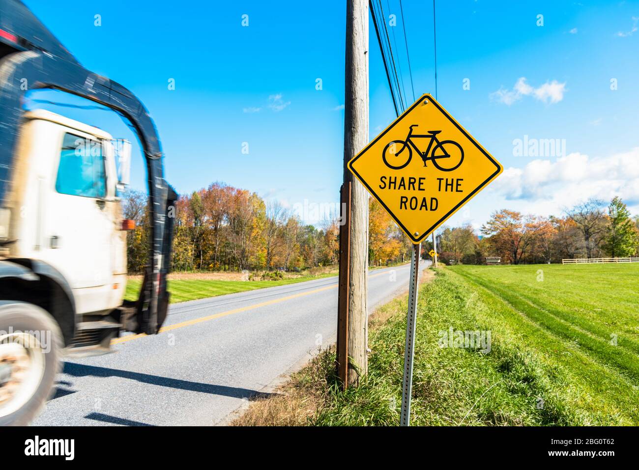 Verkehrsschild warnt Fahrer vor Fahrrädern auf einer belebten Landstraße an einem sonnigen Herbstmorgen Stockfoto