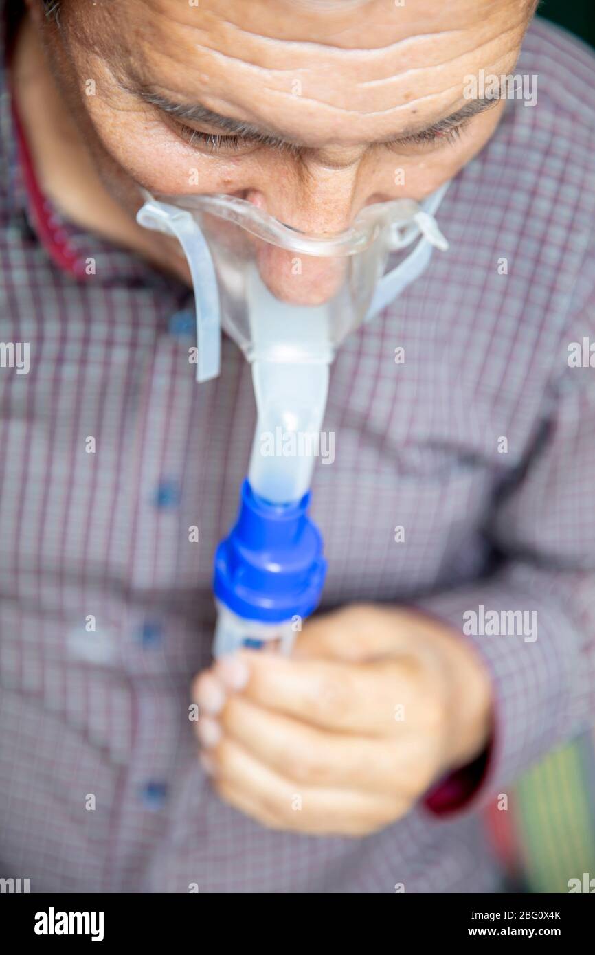 Leitender Mann, der medizinische Geräte für die Inhalation mit Atemschutzmaske verwendet, Vernebler im Zimmer Stockfoto