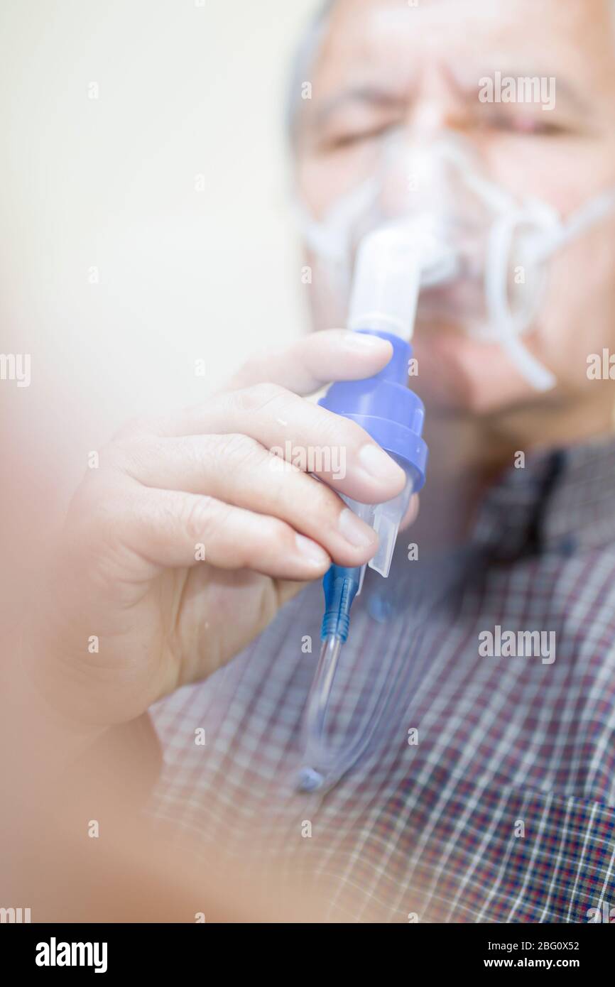 Leitender Mann, der medizinische Geräte für die Inhalation mit Atemschutzmaske verwendet, Vernebler im Zimmer Stockfoto