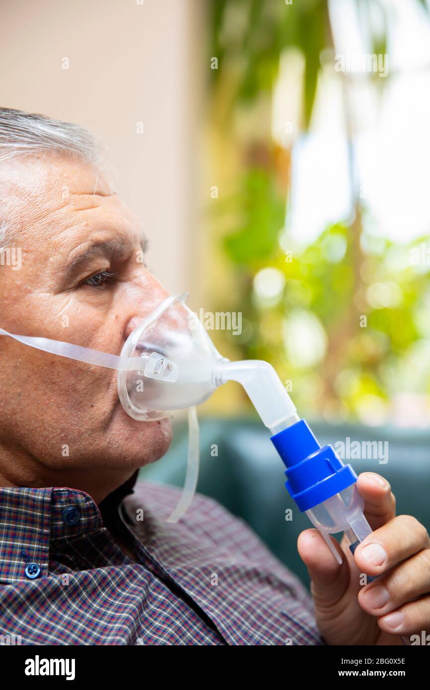 Leitender Mann, der medizinische Geräte für die Inhalation mit Atemschutzmaske verwendet, Vernebler im Zimmer Stockfoto