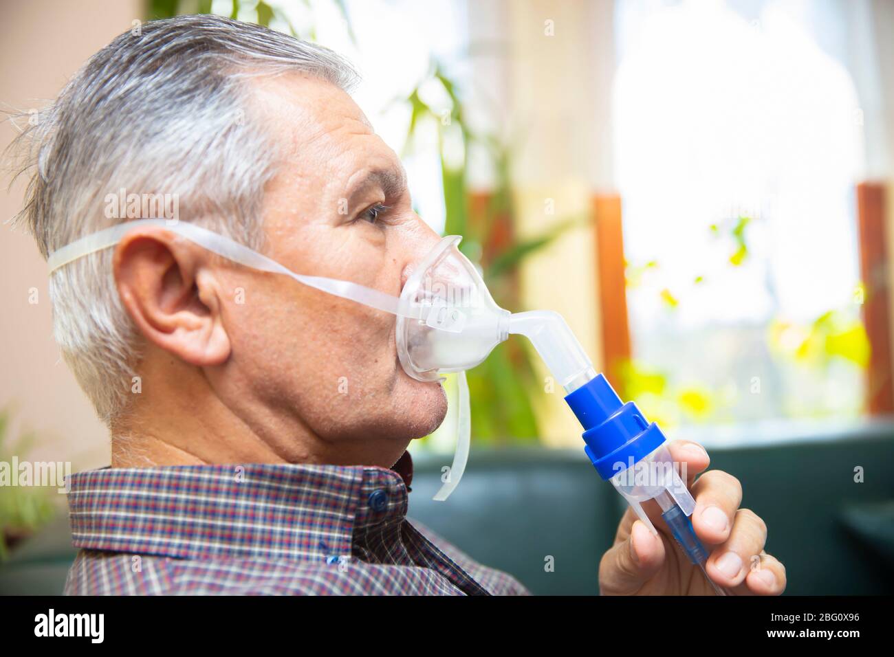 Leitender Mann, der medizinische Geräte für die Inhalation mit Atemschutzmaske verwendet, Vernebler im Zimmer Stockfoto