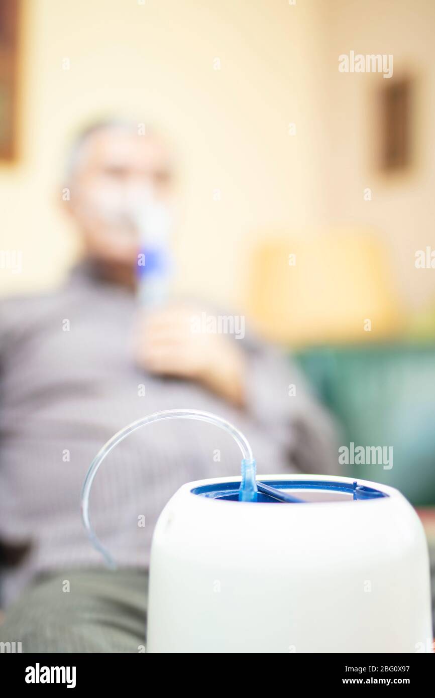 Leitender Mann, der medizinische Geräte für die Inhalation mit Atemschutzmaske verwendet, Vernebler im Zimmer Stockfoto