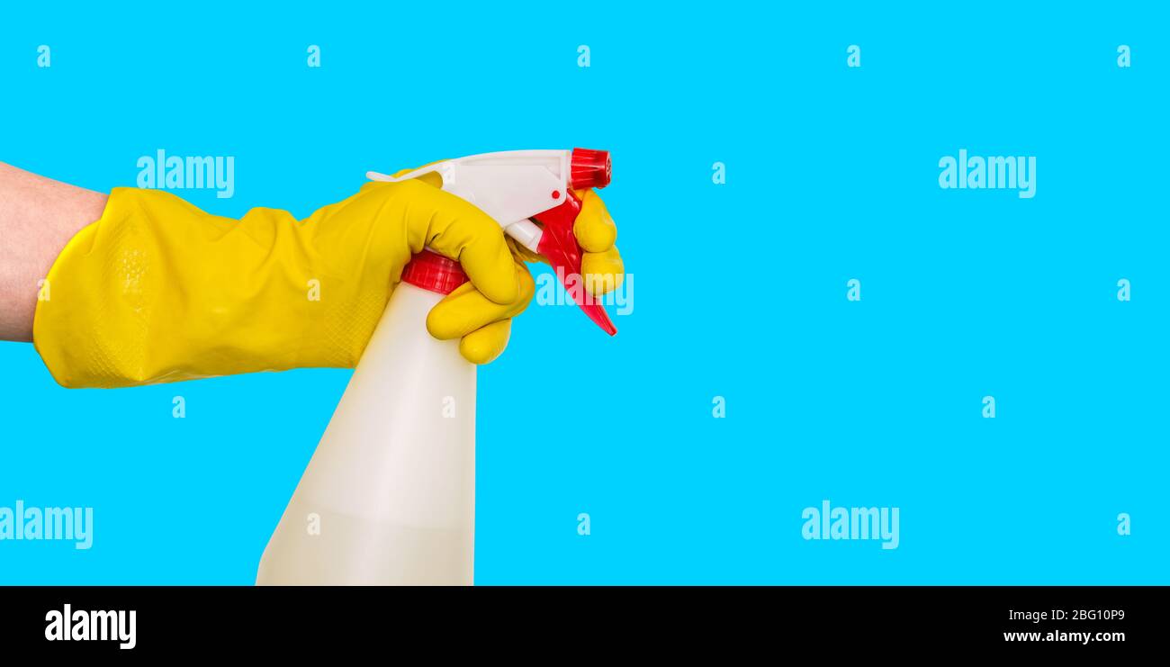 Hand in einem gelben Handschuh hält ein Spray mit einem Spender. Flasche auf blauem Hintergrund. Sprühgerät für Reinigung und Desinfektion von Büro und Haus. Seitenwie Stockfoto