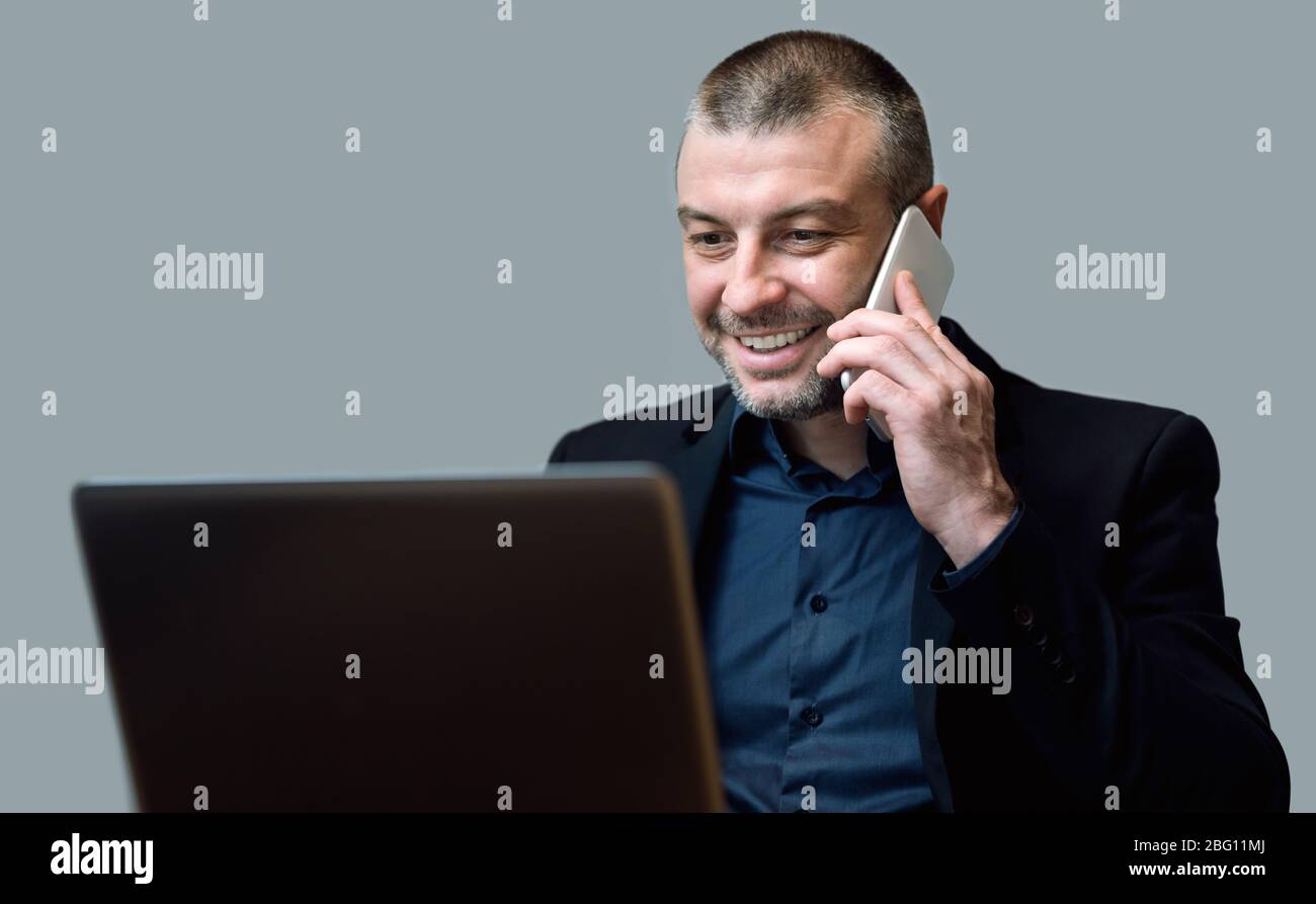 Geschäftsmann Arbeitet Auf Laptop Im Gespräch Auf Handy Über Grauen Hintergrund Stockfoto