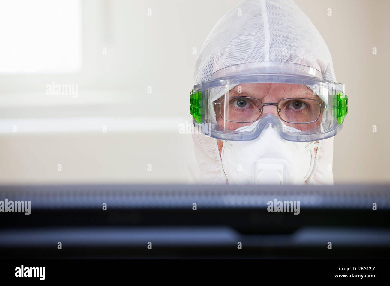 Gesicht eines müden Arztes mit Schutzkleidung eine medizinische Maske hinter einem Computermonitor im Krankenhaus - selektiver Fokus Stockfoto
