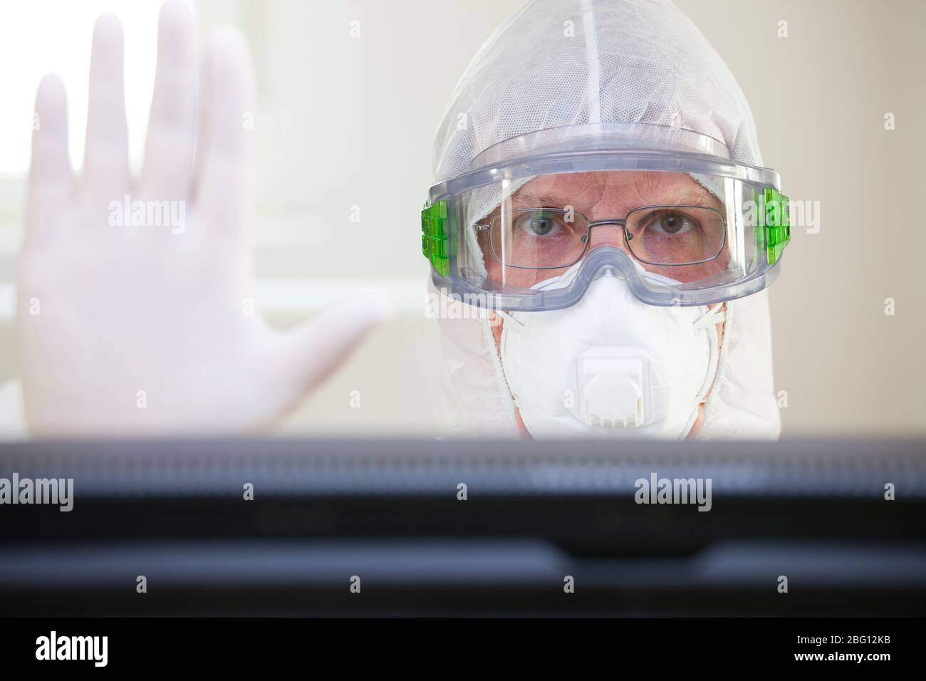 Arzt mit Schutzkleidung wegen Covid-19 Gesturing Stop während des Sitzens hinter einem Computerbildschirm in einem Krankenhaus - selektive Fokussierung Stockfoto