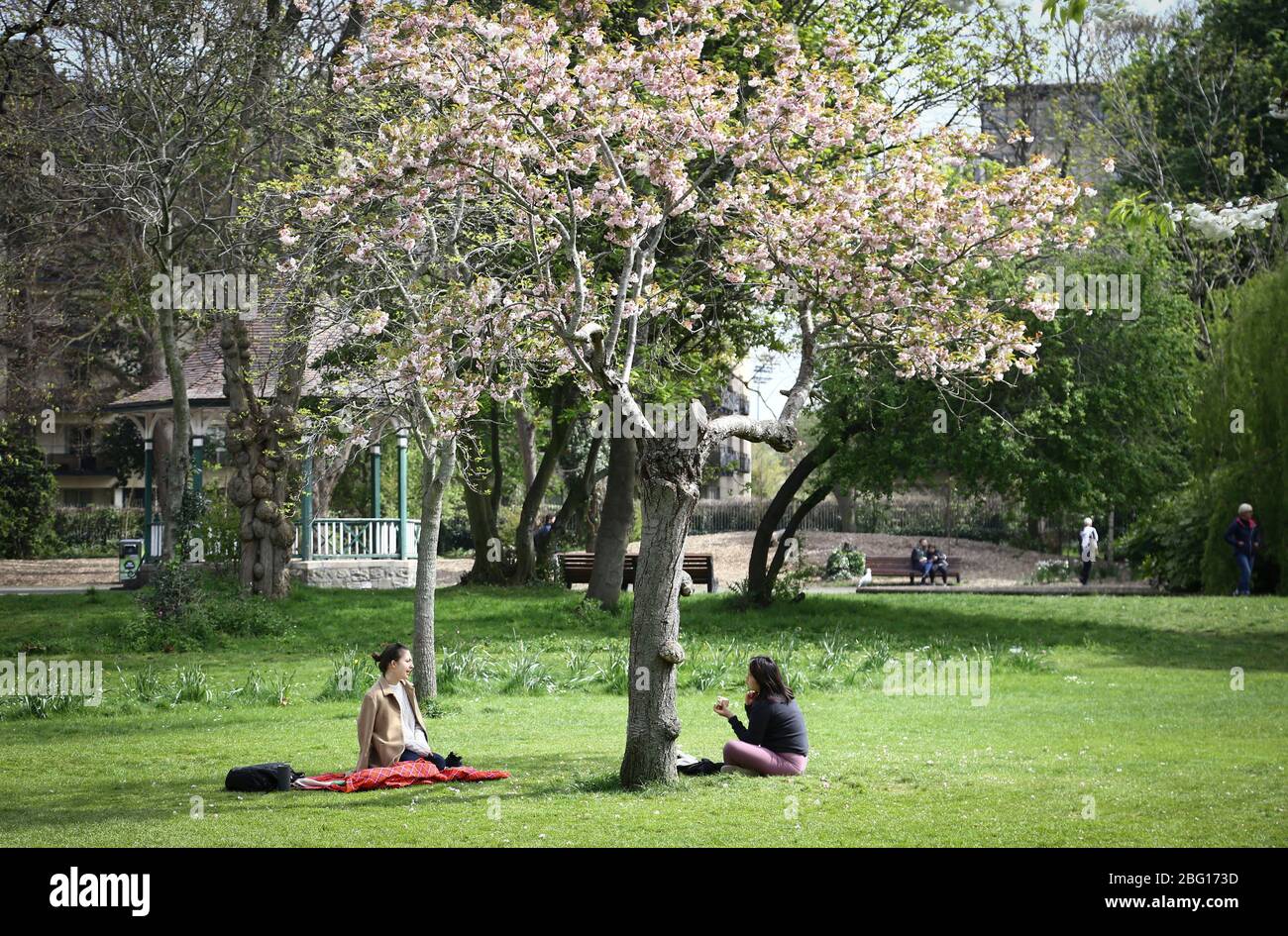 Dublin, Irland - 19. April 2020: Zwei Frauen halten sich an die Regeln der sozialen Distanz, während sie im Herbert Park picknicken. Stockfoto