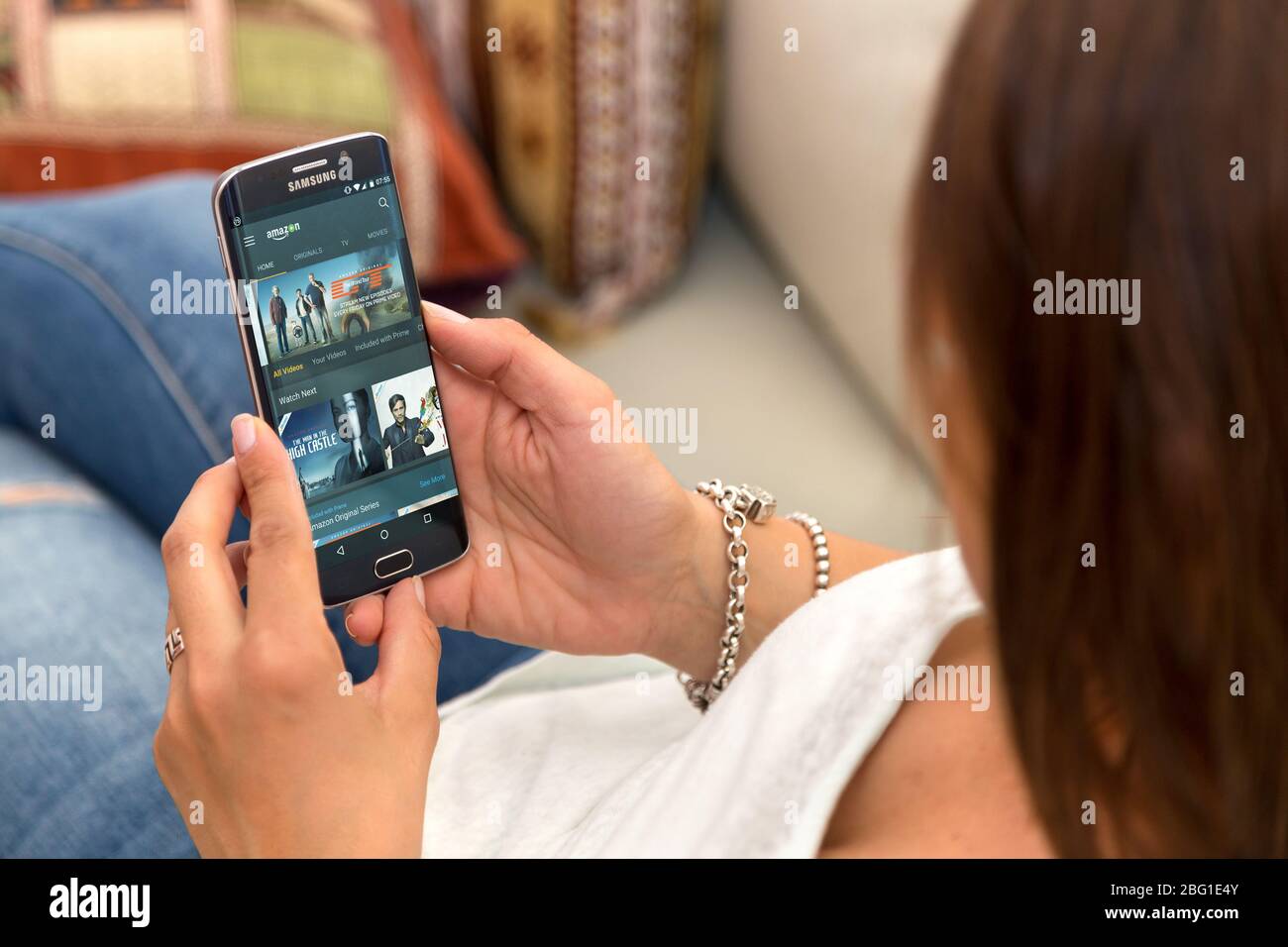 Junge einsame Frau, die im Sessel ruht und mit Amazon Prime Web auf dem Bildschirm Handy hält. ROSARIO, ARGENTINIEN - 28. OKTOBER 2017 Stockfoto