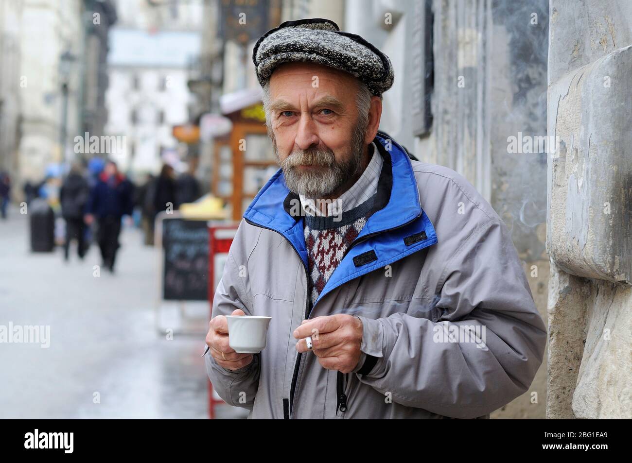 Ein alter trauriger Mann, der auf der Straße steht, mit einer Kaffe und einer Zigarette in den Händen Stockfoto