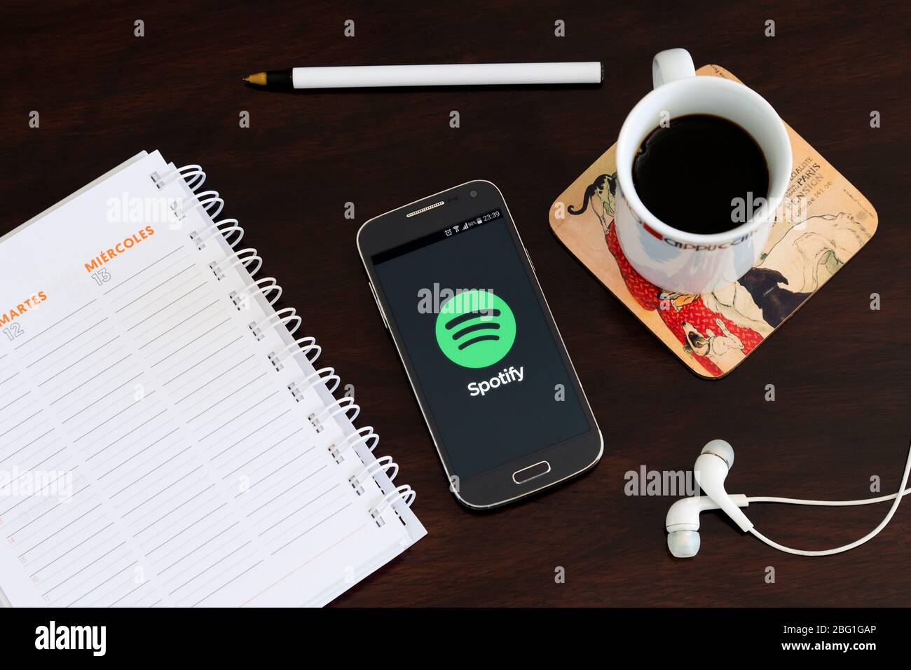 Mobiltelefon über den Schreibtisch mit der Spotify-Anwendung auf dem Bildschirm. Musik-App streamen. Stockfoto