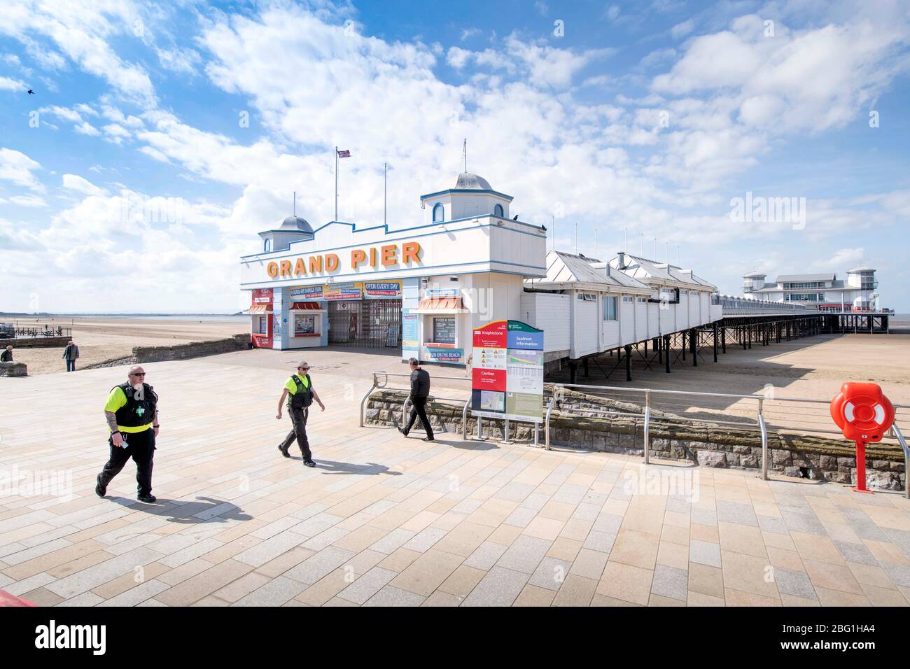 Zwei gemeinschaftliche Straßenwärter passieren den Grand Pier in Weston-super-Mare während der Coronavirus-Sperre, Großbritannien Stockfoto