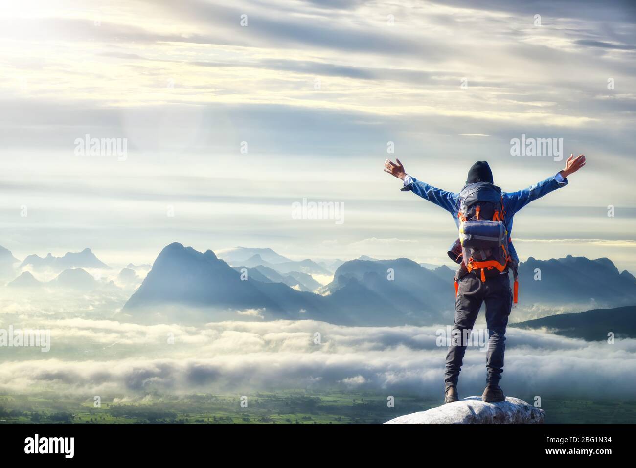 Mann mit Rucksack, Reisender oder Entdecker auf dem Gipfel des Berges oder der Klippe stehend und auf das Tal schauend. Konzept der Entdeckung, Erforschung, Wandern, Advent Stockfoto