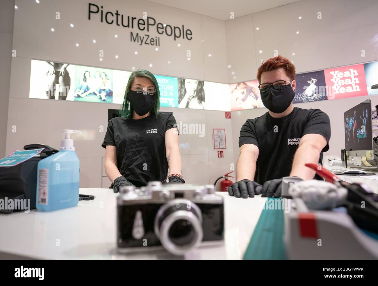 20. April 2020, Hessen, Frankfurt/Main: Sarina Weber (l.) und Sven  Fleischmann stehen hinter der Theke in einem Laden für Porträtfotografie im  Einkaufszentrum 'MyZeil', das nach wochenlanger Schließung aufgrund der  Corona-Pandemie wieder eröffnet