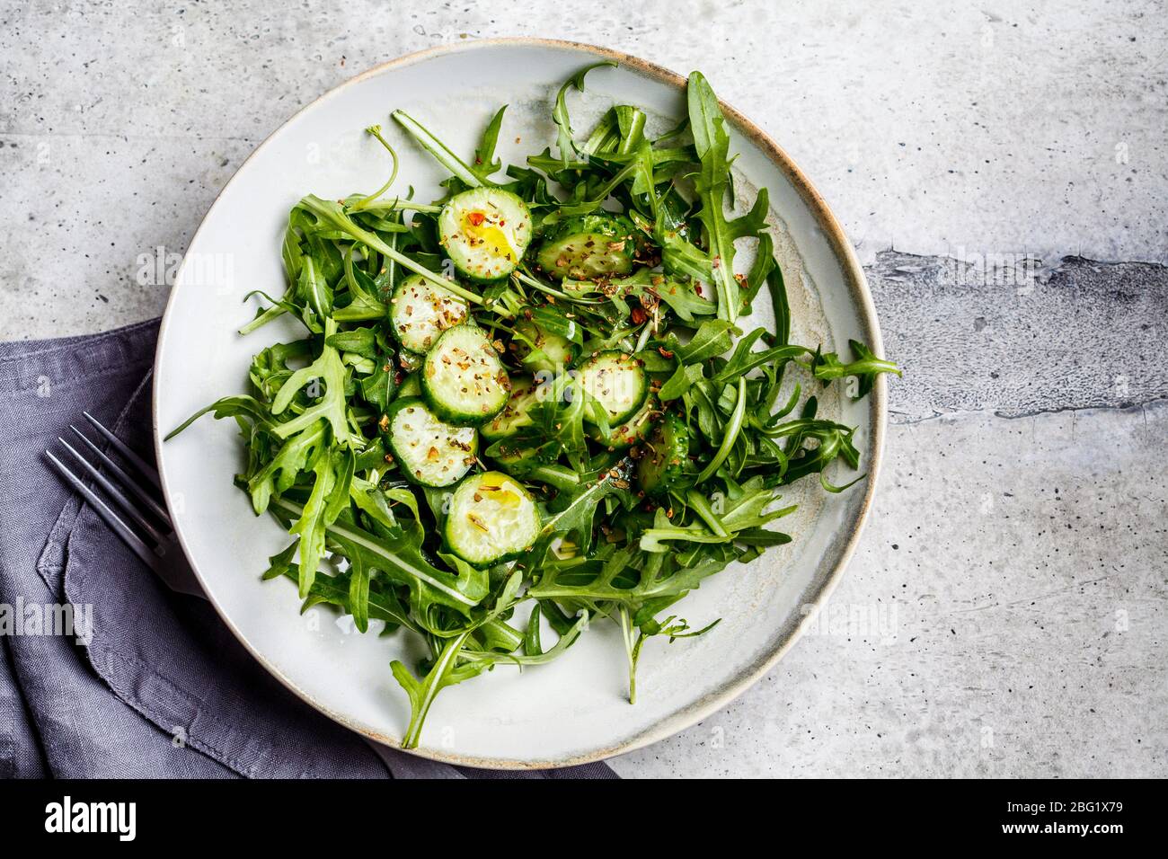 Grüner Salat aus Rucola und Gurken mit Öl und Gewürzen in einer großen grauen Schüssel. Stockfoto