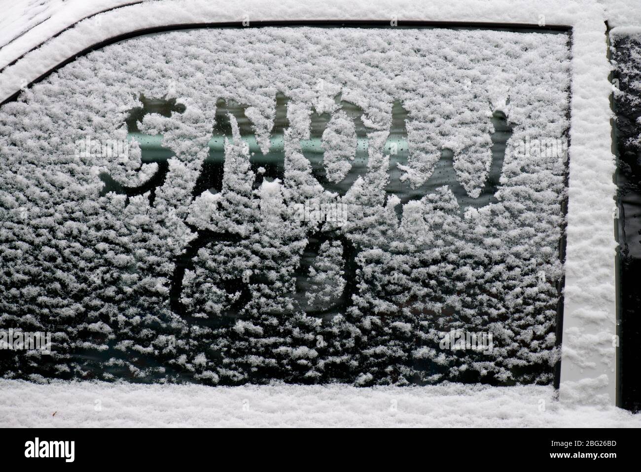 Ein Autofenster mit Staub von Schnee bedeckt mit den Worten Schnee gehen darin geschrieben Stockfoto