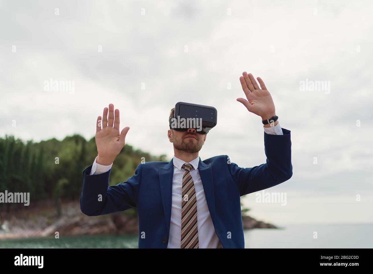 Businessman nutzt VR-Headset, um eine virtuelle Realität auf dem Hintergrund des Meeres darzustellen Stockfoto
