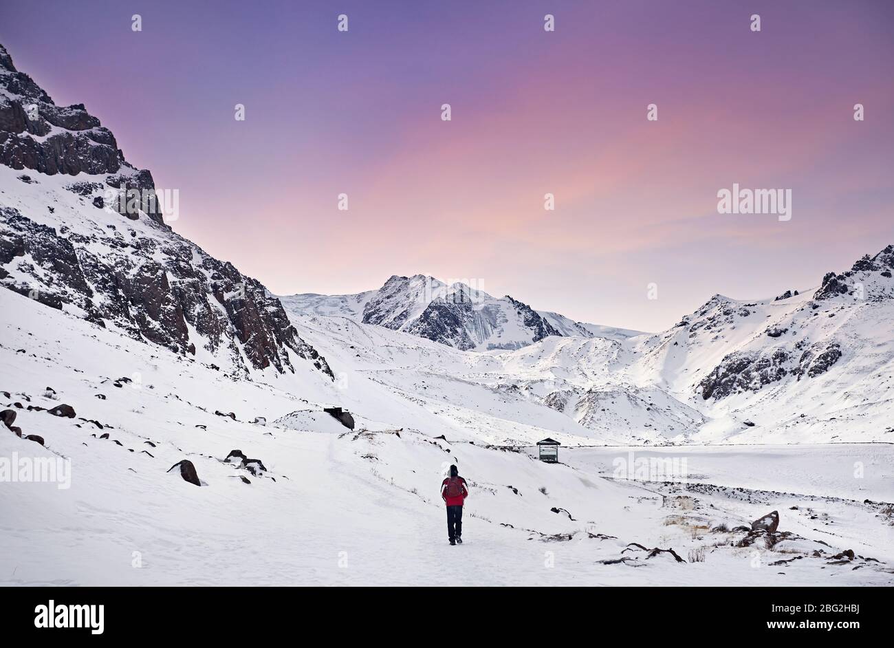 Wanderer mit roten Rucksack wandern rund um schneebedeckten Berge am purpurroten Himmel Hintergrund. Freiheit von trekking Konzept. Stockfoto