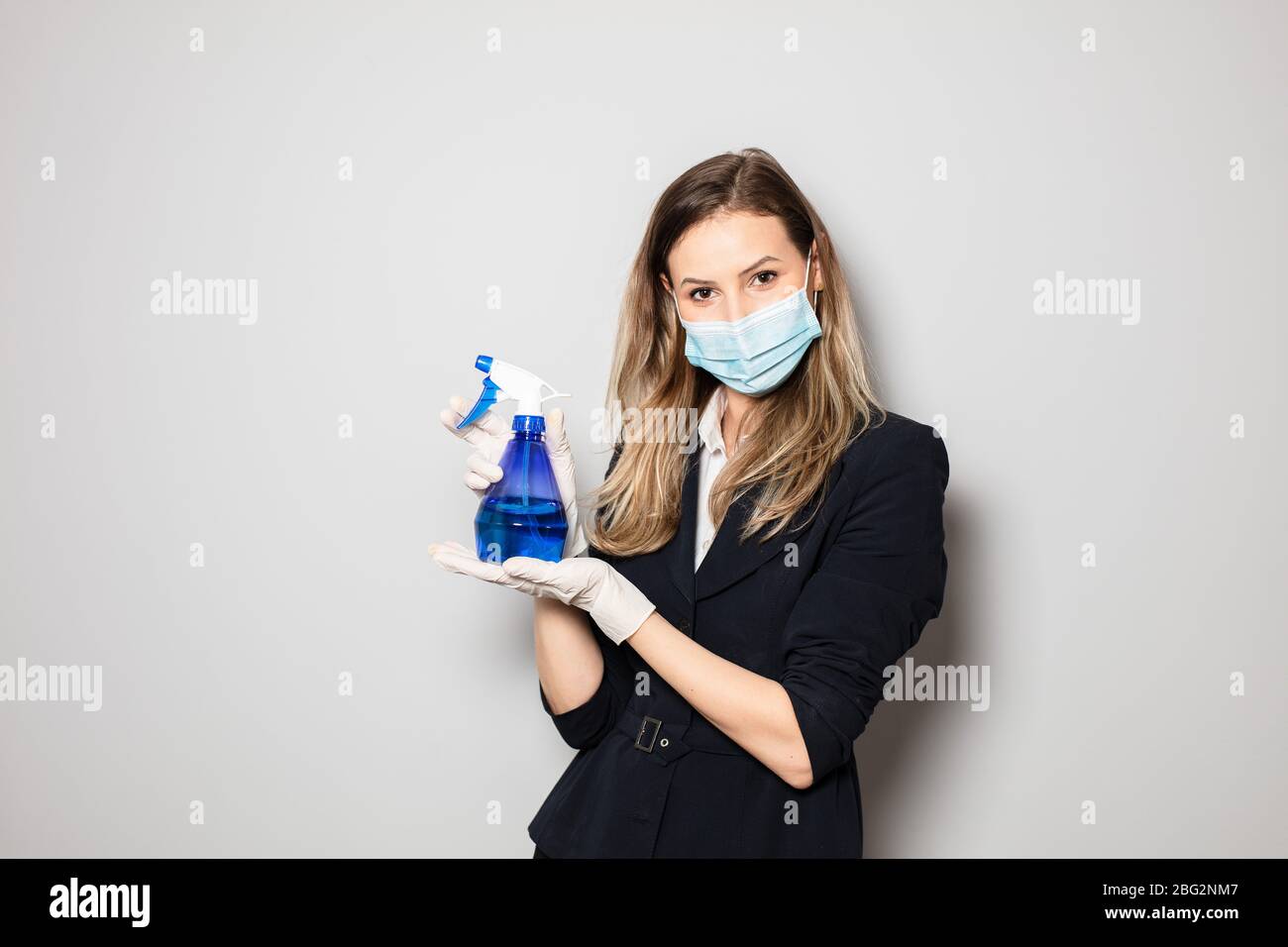 Elegante Geschäftsfrau mit Maskenschutz und Handschuhen, die eine Flasche Desinfektion in den Händen halten Stockfoto
