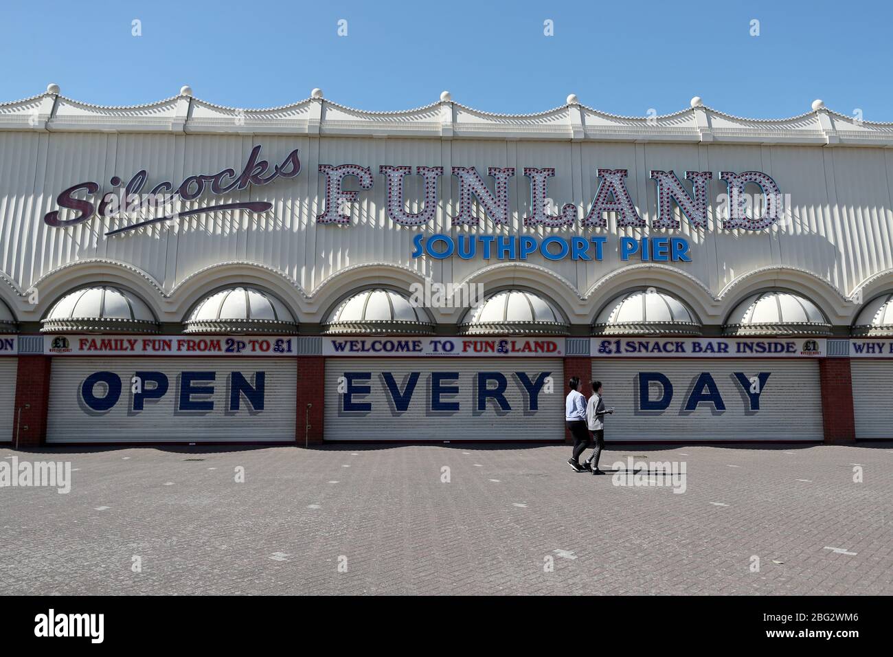Zwei Personen gehen an den geschlossenen Fensterläden vorbei, mit einem Schild mit der Aufschrift "Open Every Day", am Silcocks Funland und Pier, Southport, während Großbritannien weiterhin gesperrt wird, um die Ausbreitung des Coronavirus einzudämmen. Stockfoto