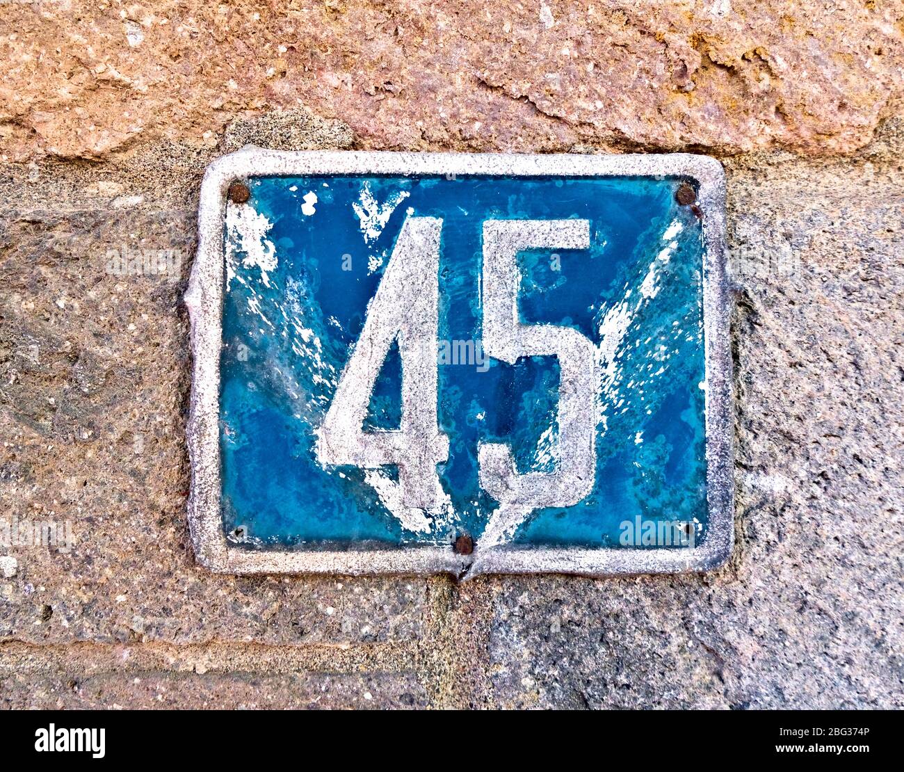 45 (fünfundvierzig) ein verbeultes Schild mit Hausnummer auf einer Steinmauer. Stockfoto