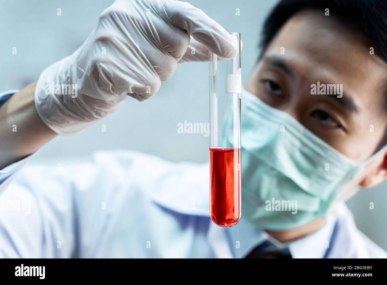Nahaufnahme eines asiatischen männlichen Wissenschaftlers in einer einheitlichen Holding-Laborflasche mit roter chemischer Lösung. Chemie, Biologische, Toxikologie, Konzept Stockfoto