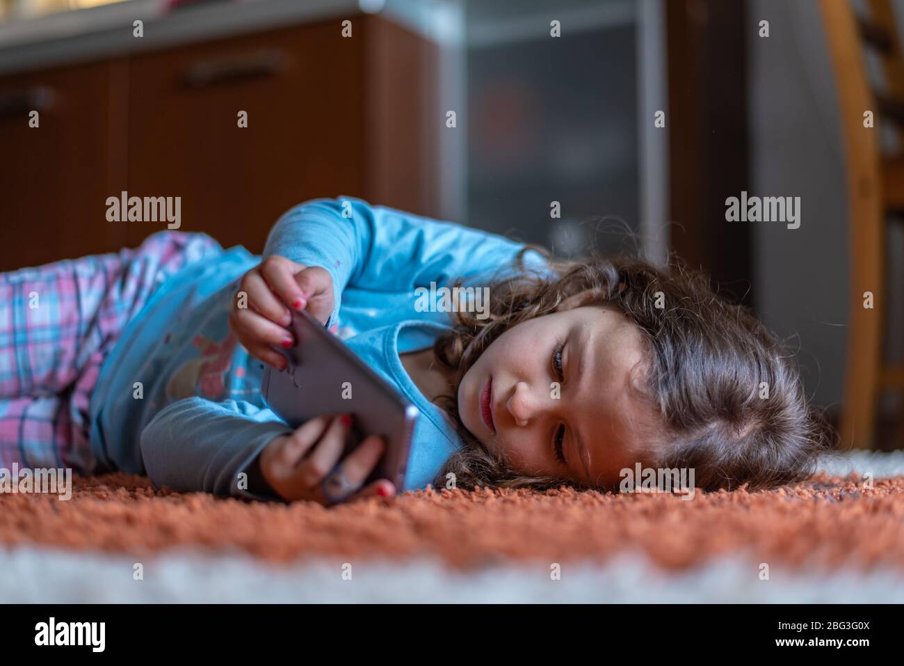 Nettes kleines glückliches Mädchen, das sich auf die Verwendung suchen digitales Smartphone-Handy im Wohnzimmer zu Hause. Familie Aktivität Konzept. Stockfoto