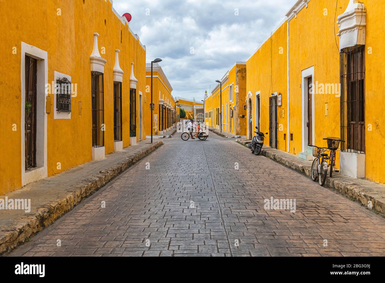 Stadtbild mit Menschen auf einem Dreirad in den bunten gelben Straßen mit kolonialer Architektur, Izamal, Mexiko. Stockfoto