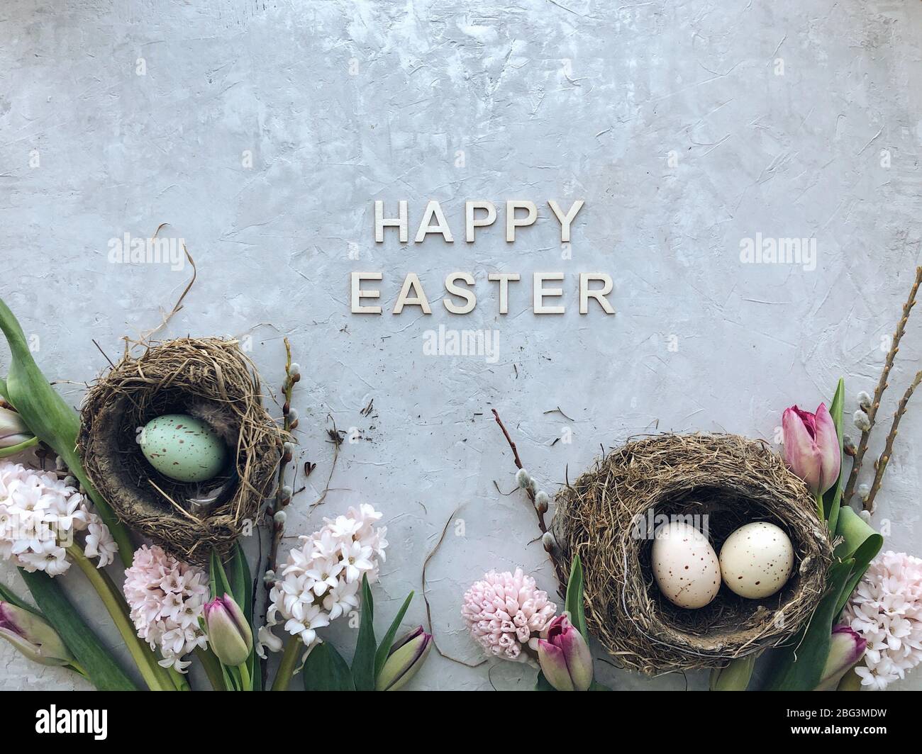 Ostereier in Nestern mit Blumen und Frohe Ostern Text Stockfoto