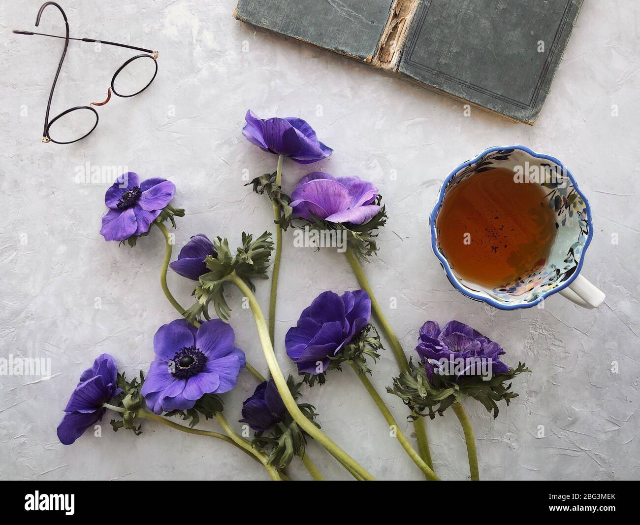 Anemone Blumen, Tasse Tee, Brille und ein Buch Stockfoto