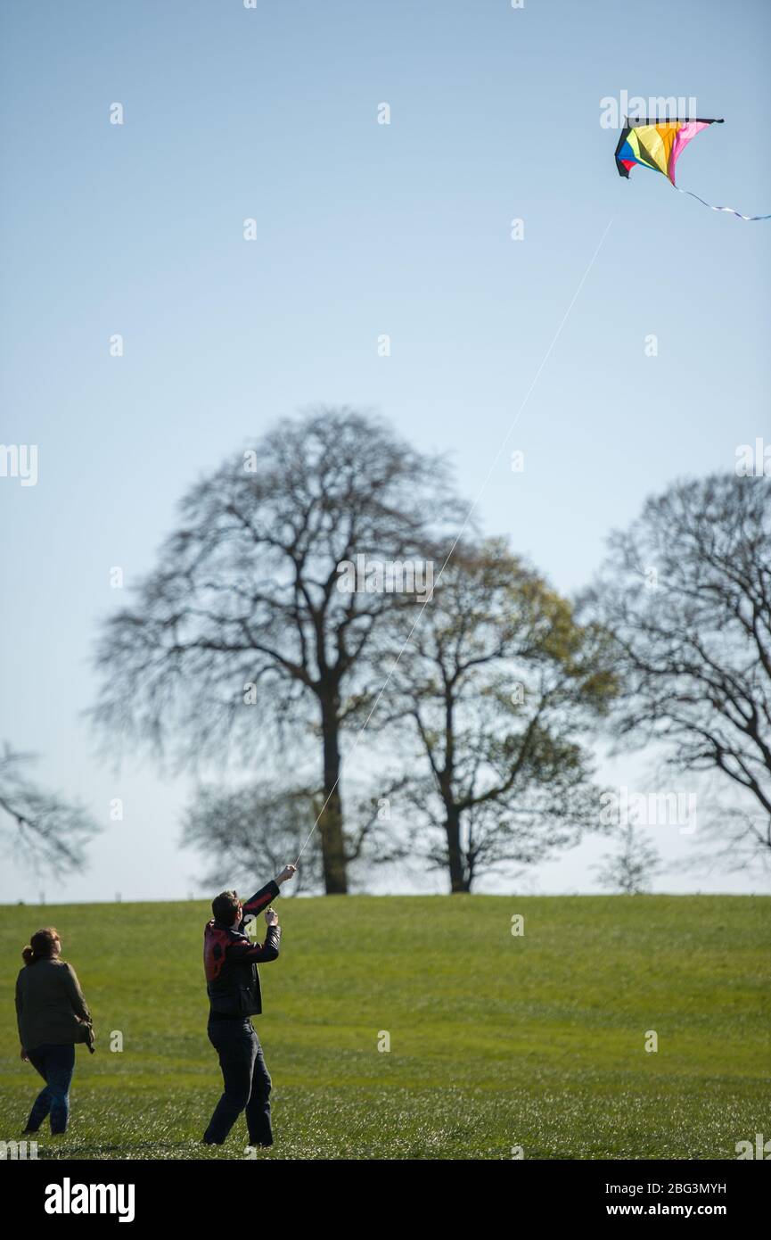 Bishopbriggs, Glasgow, Großbritannien. April 2020. Im Bild: Rachel und Scott nutzen ihre vorgesehene Übungszeit und nutzen einen schönen sonnigen und windigen Tag, um ihren Drachen zu fliegen. Ein blauer Himmel und ein grünes Feld bilden eine perfekte Kulisse für Drachenfliegen. Quelle: Colin Fisher/Alamy Live News Stockfoto