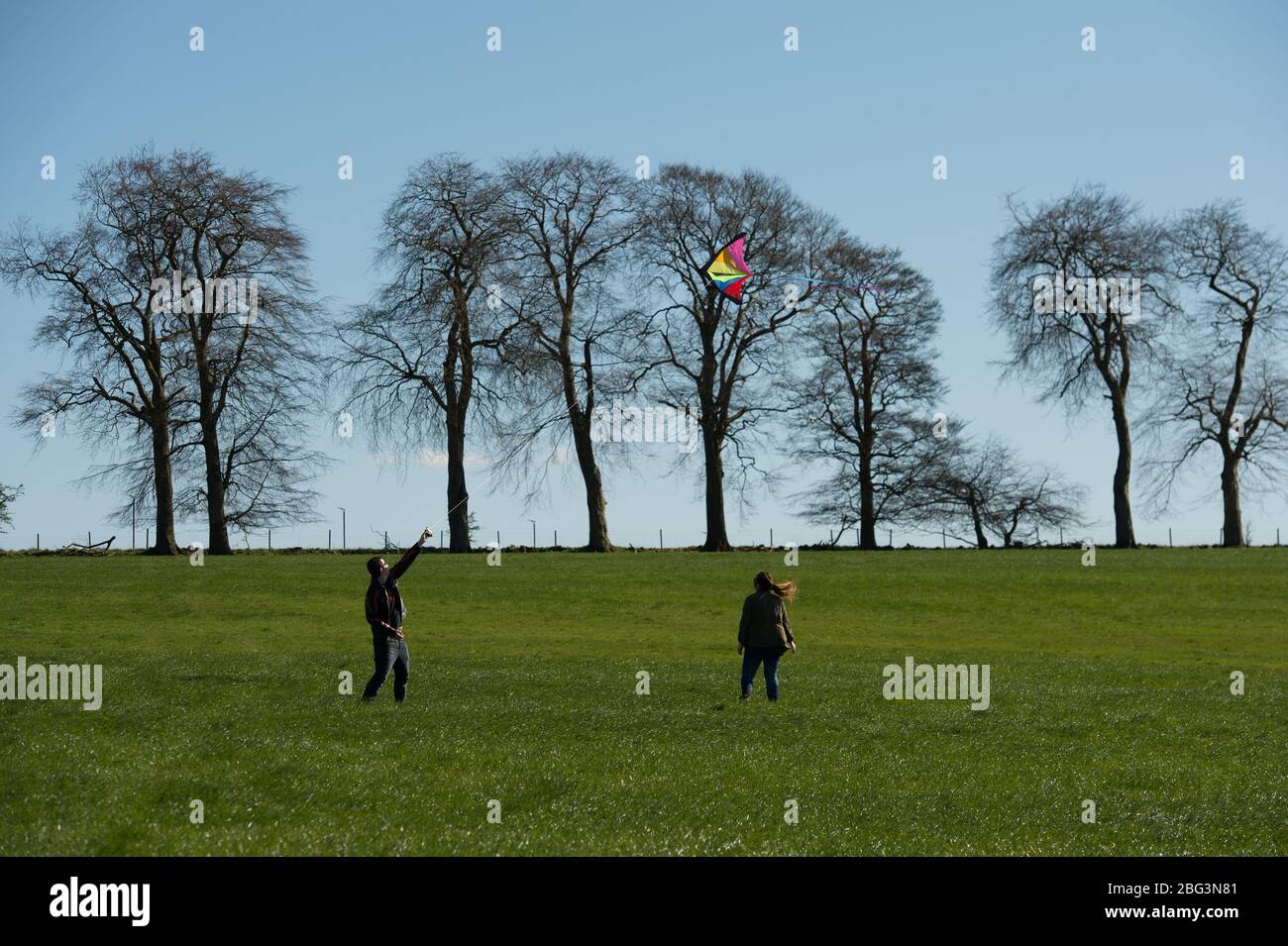 Bishopbriggs, Glasgow, Großbritannien. April 2020. Im Bild: Rachel und Scott nutzen ihre vorgesehene Übungszeit und nutzen einen schönen sonnigen und windigen Tag, um ihren Drachen zu fliegen. Ein blauer Himmel und ein grünes Feld bilden eine perfekte Kulisse für Drachenfliegen. Quelle: Colin Fisher/Alamy Live News Stockfoto