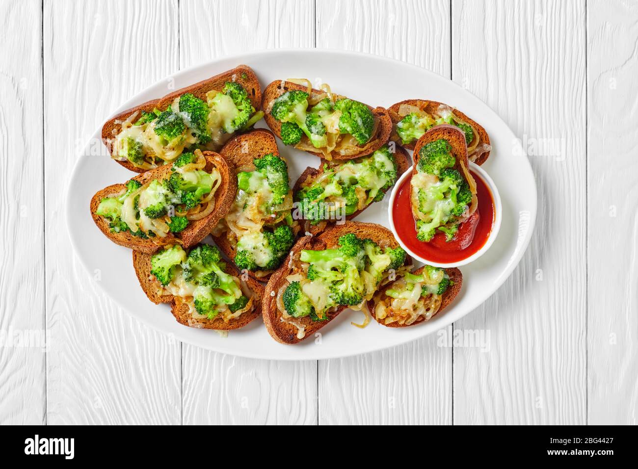 Brokkoli schmilzt offene vegane Sandwiches mit geröstetem Brokkoli auf geröstetem Roggenbrot mit geschmolzenem Provolonkäse auf einem weißen Teller mit Ketchup Stockfoto