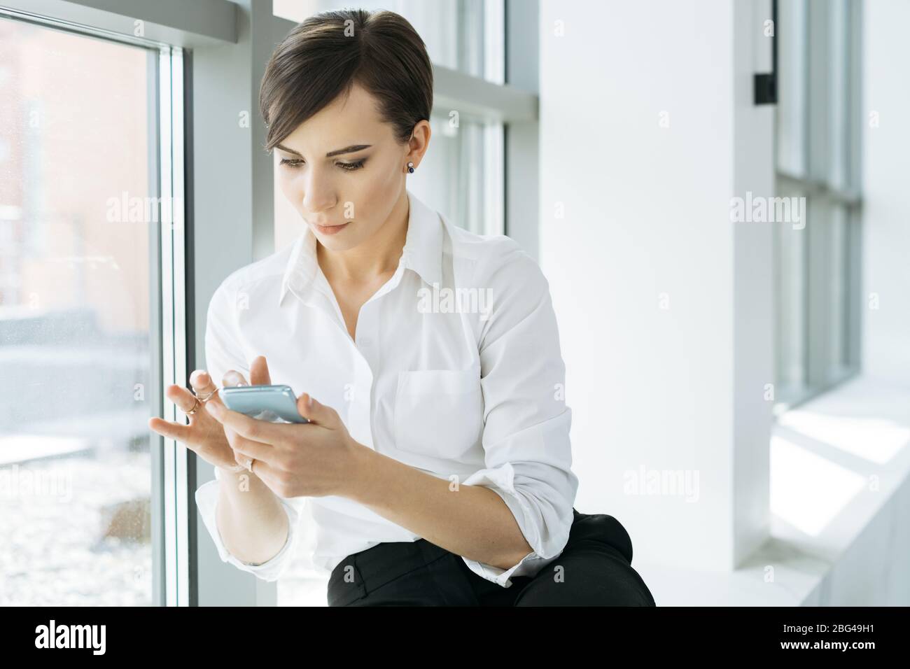 Geschäftsfrau sitzt auf einer Fensterbank mit ihrem Handy Stockfoto