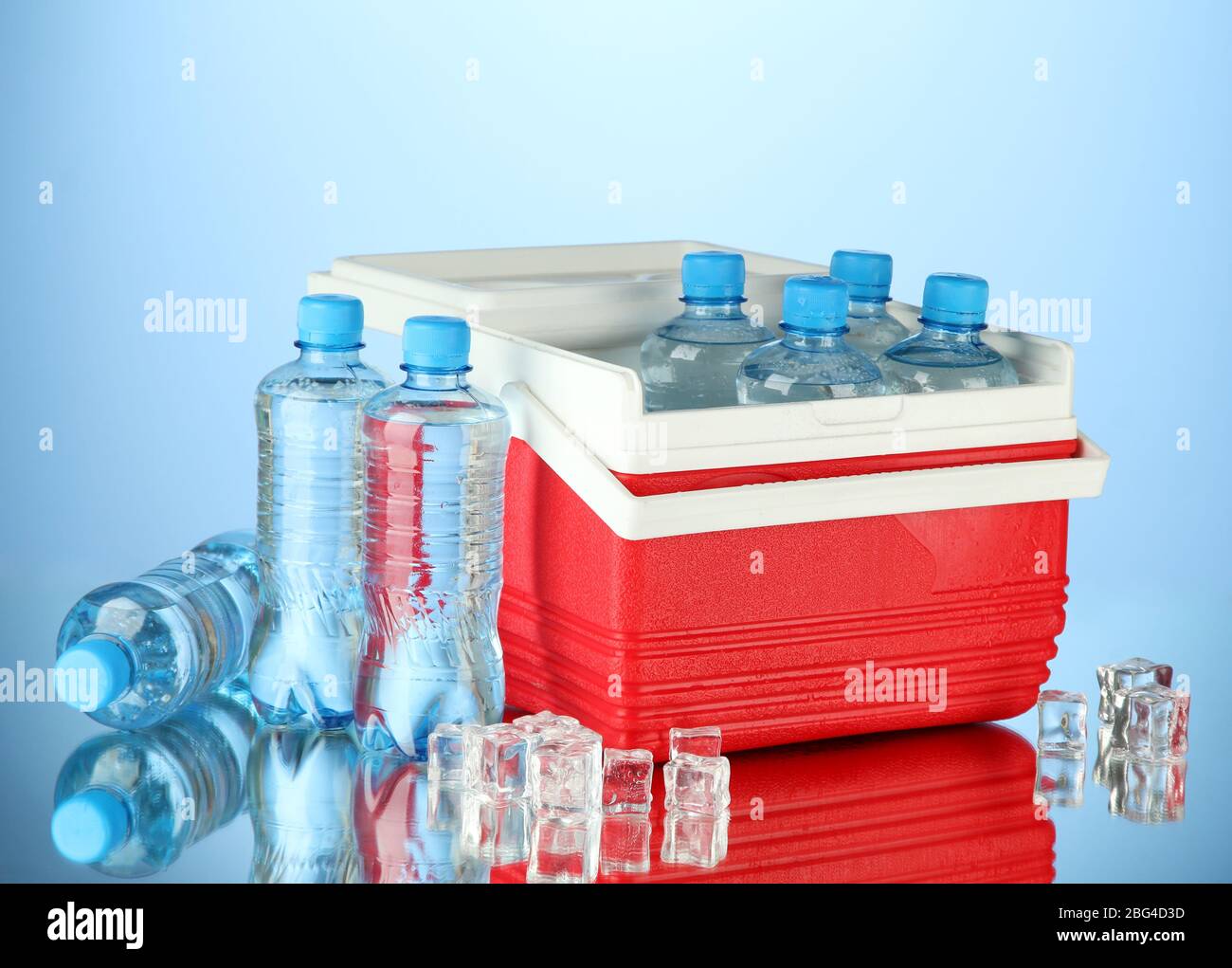 Reisekühlschrank mit Wasserflaschen und Eiswürfeln, auf blauem Hintergrund Stockfoto