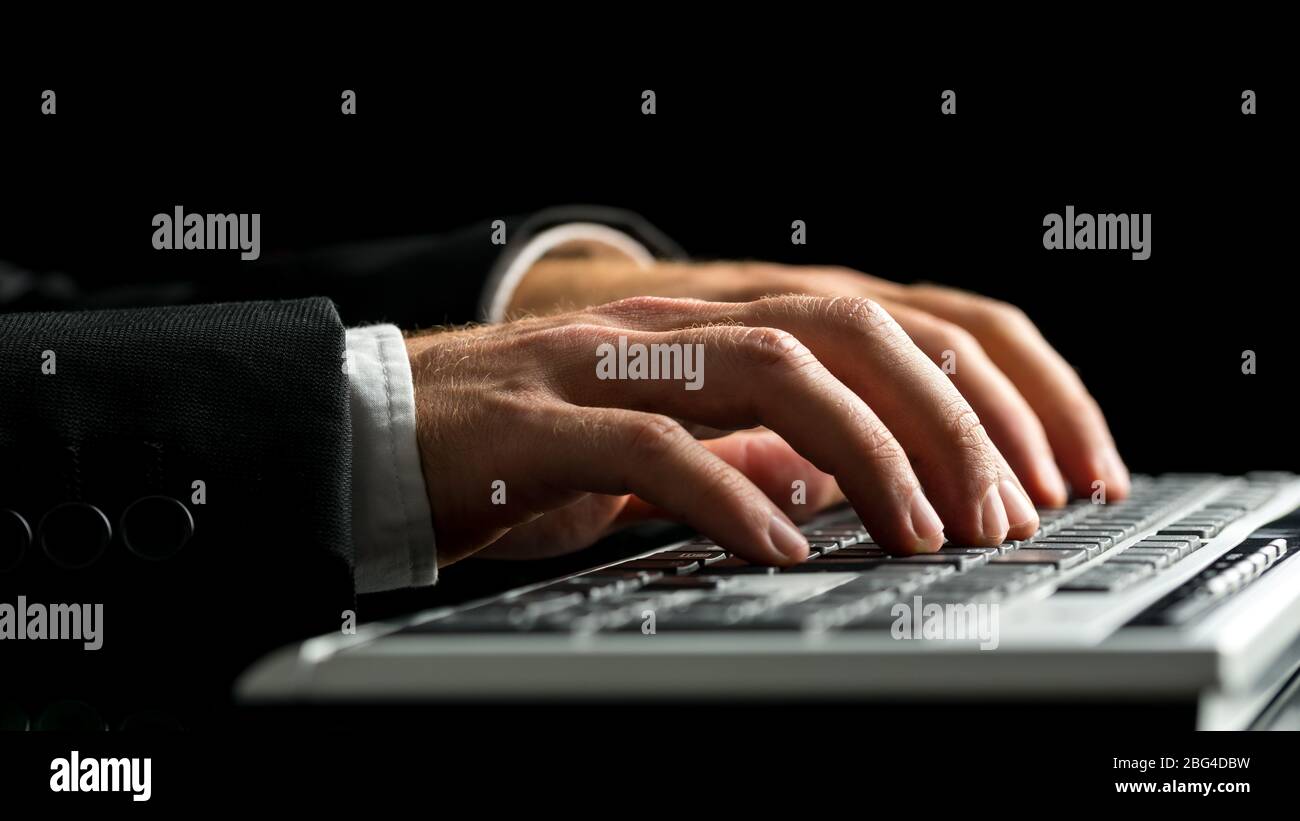 Hände eines Geschäftsmannes, der am Computer arbeitet, indem er auf der Tastatur Schreibarbeit macht, auf schwarzem Hintergrund. Stockfoto