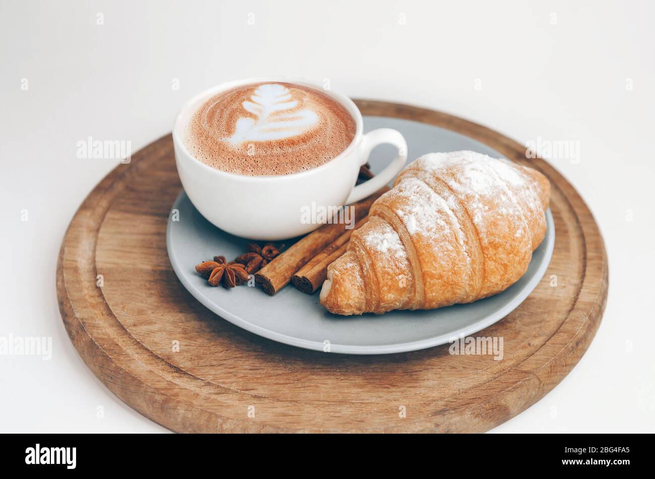 Frisch gebackenes Croissant mit Kaffeetasse und Latte Art, Zimt und Sternanis Stockfoto